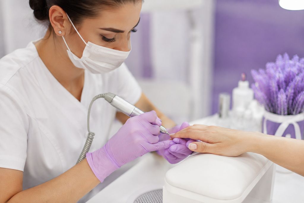 Prothésiste ongulaire utilisant une ponceuse électrique sur les mains d'une cliente, ambiance salon professionnelle, éclairage doux