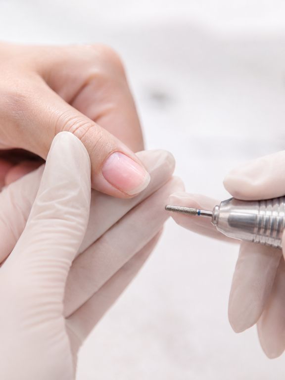 Prothésiste inspectant un ongle naturel légèrement transparent après ponçage, signal d'alerte visuel pour stopper le travail