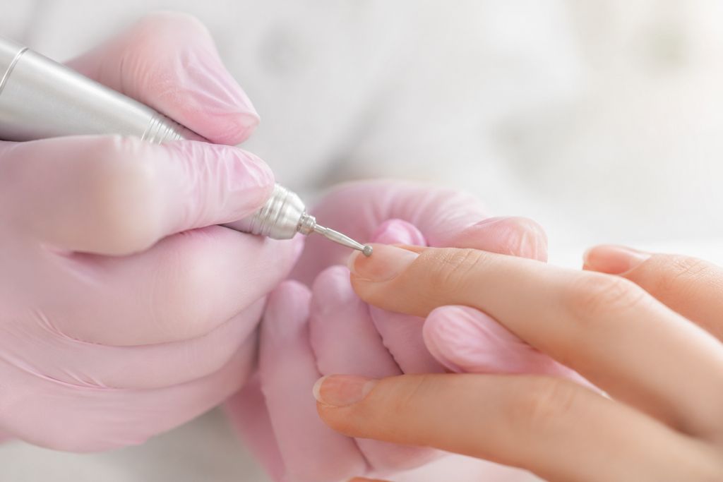 Gros plan sur une main tenant une ponceuse à ongles stylo sans appuyer sur la plaque naturelle, geste technique correct